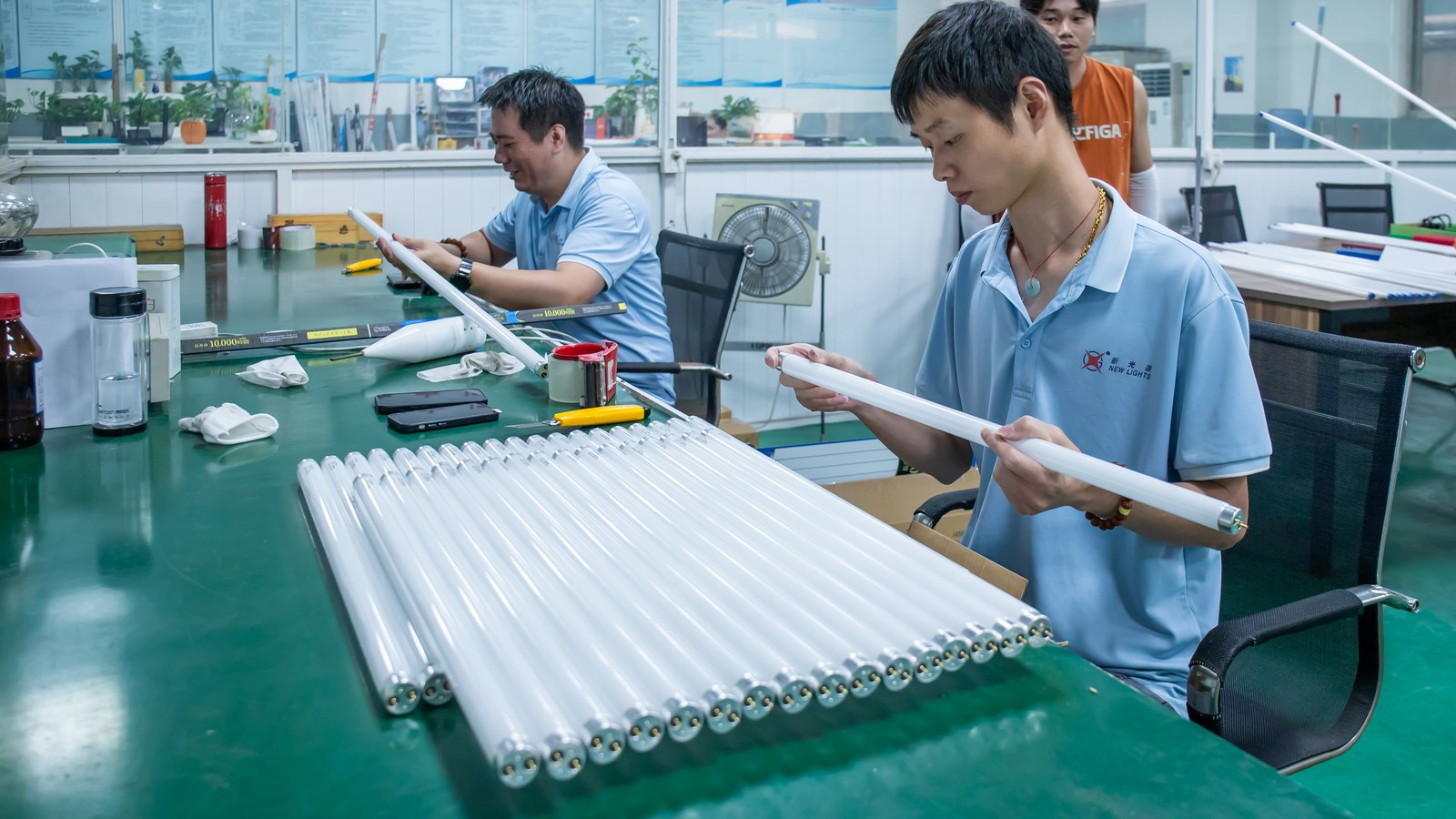 New Lights staff visually inspecting LED tube assemblies at a worktable